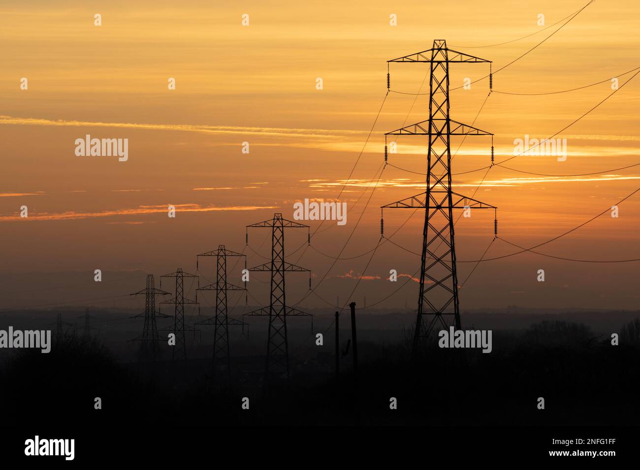 Row of electricity pylons silhouette against orange sky at sunset, UK. Theme of energy usage, power, bills, rising costs, power grid Stock Photo