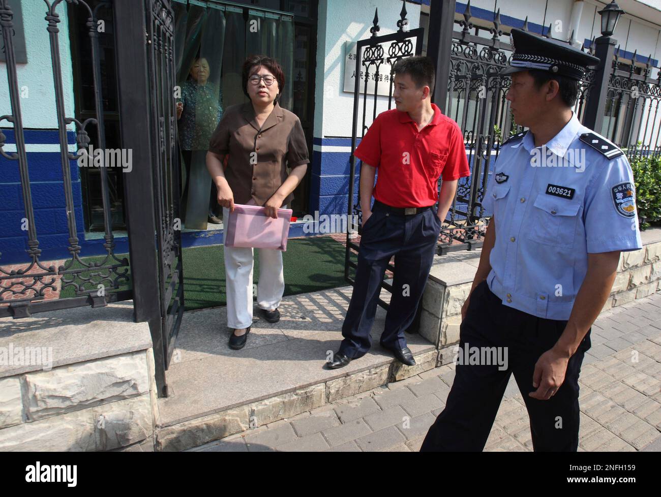 A Chinese police officer and a plain clothes security personnel, in red  watch as Sun Liwei walk out of a Public Security Bureau where she tried to  apply for a protest permit