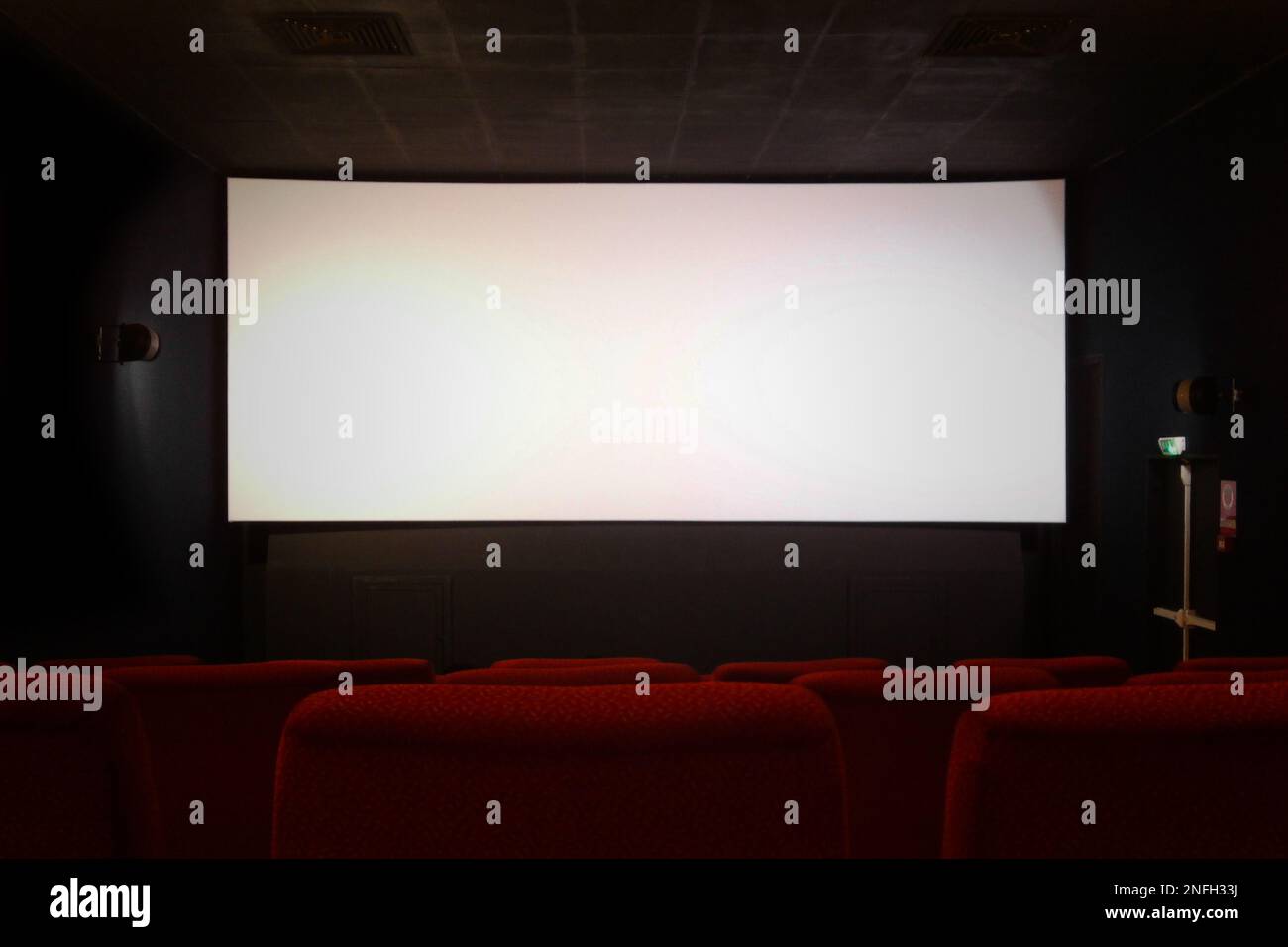 Row of red seats in a movie theater with the white few minutes before the begin of the movie. The white screen can eventually be field with anything Stock Photo