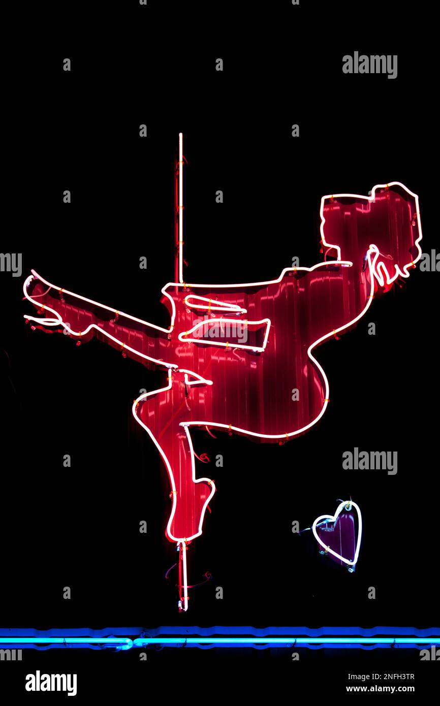 Close-up on a red neon light shaped into a woman doing pole dancing. Stock Photo