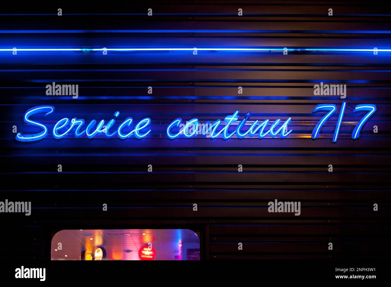 Close-up on a blue neon light outside a diner shaped into the French short phrase 'Service continu 7/7' meaning 'Continuous service 7/7' in English. Stock Photo