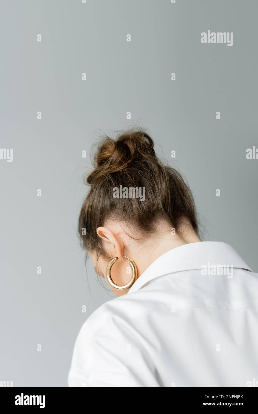 back view of young woman in golden hoop earring and white shirt isolated on grey,stock image Stock Photo