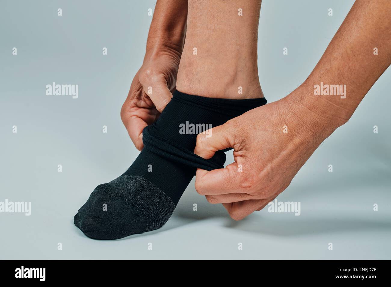 closeup of a man putting on a compression sock, on an offwhite