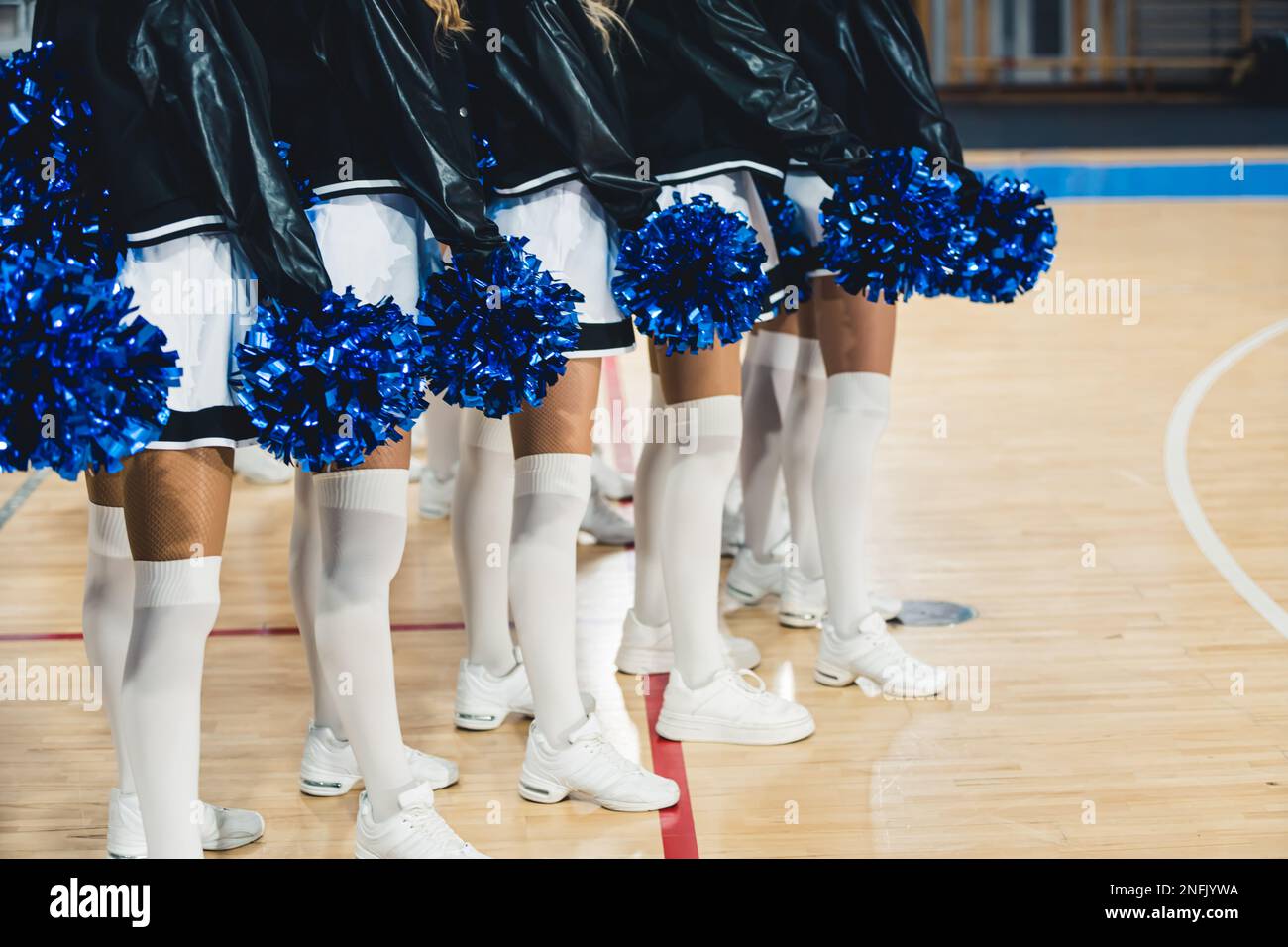 cheerleaders wearing white sneakers, tights, skirts, black jackets and blue  pom-poms, arena. High quality photo Stock Photo - Alamy