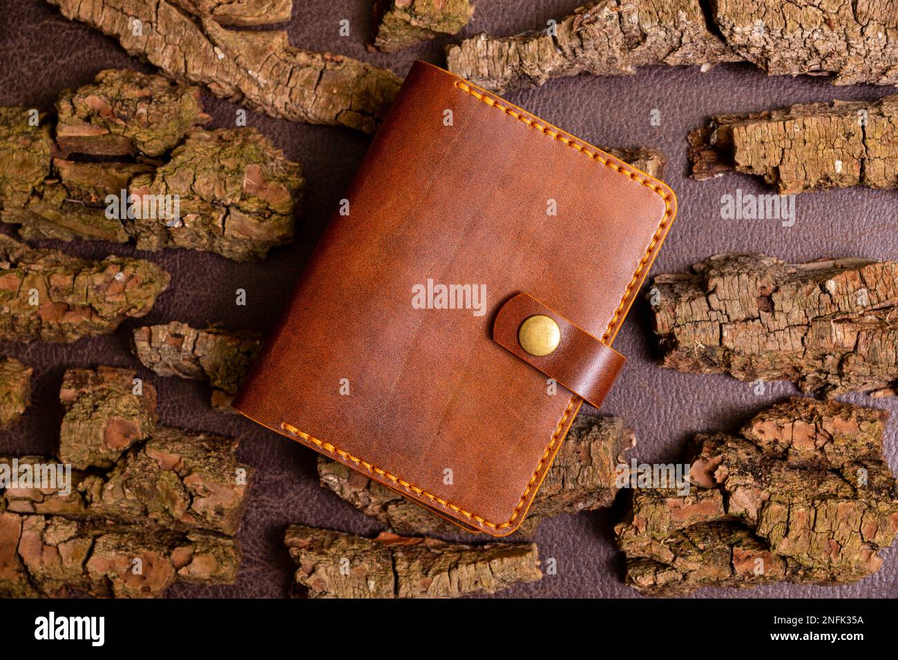 Closed brown mens wallet for cash and credit cards on leather background with pine bark. Stock Photo