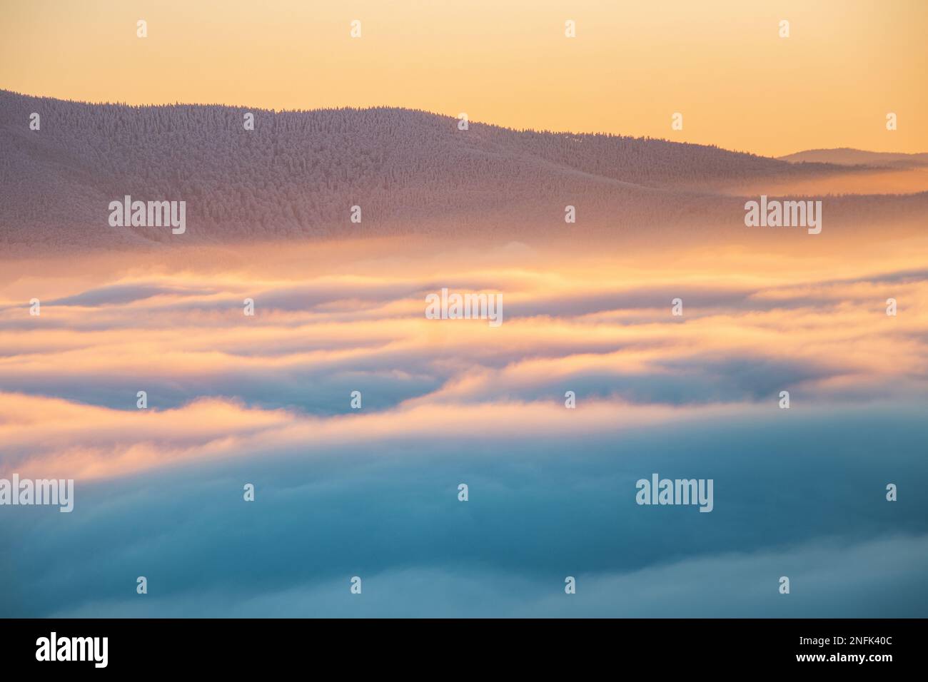 View of sea of clouds colored in the soft orange-pink hue of the morning sun. Peaks of the mountains rising out of this impermeable curtain. Sense of Stock Photo