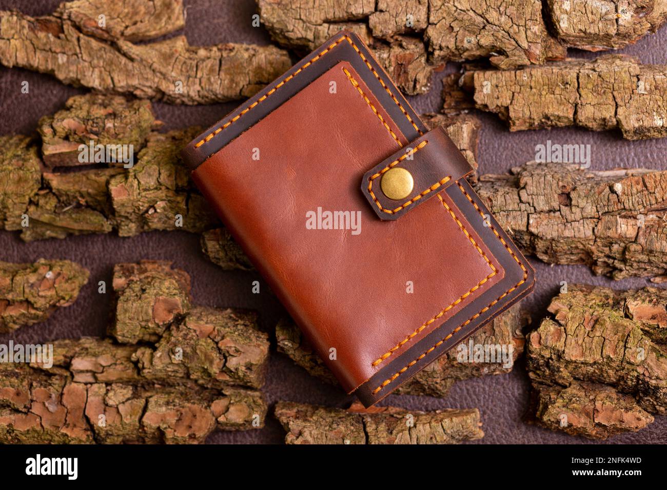 Closed brown mens wallet with money and credit cards on leather background with pine bark. Stock Photo