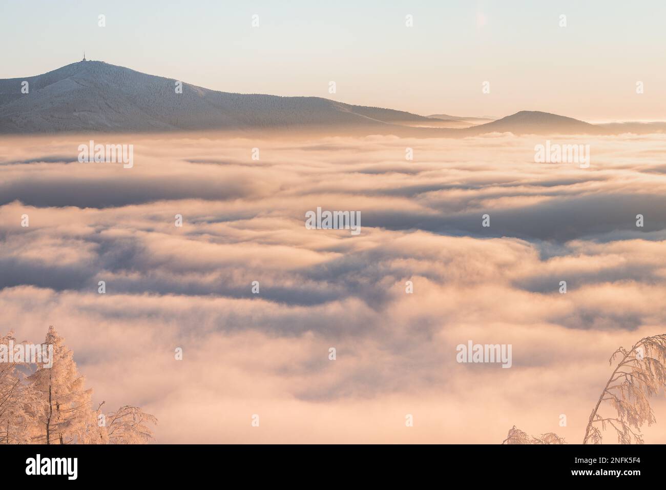 View of sea of clouds colored in the soft orange-pink hue of the morning sun. Peaks of the mountains rising out of this impermeable curtain. Sense of Stock Photo