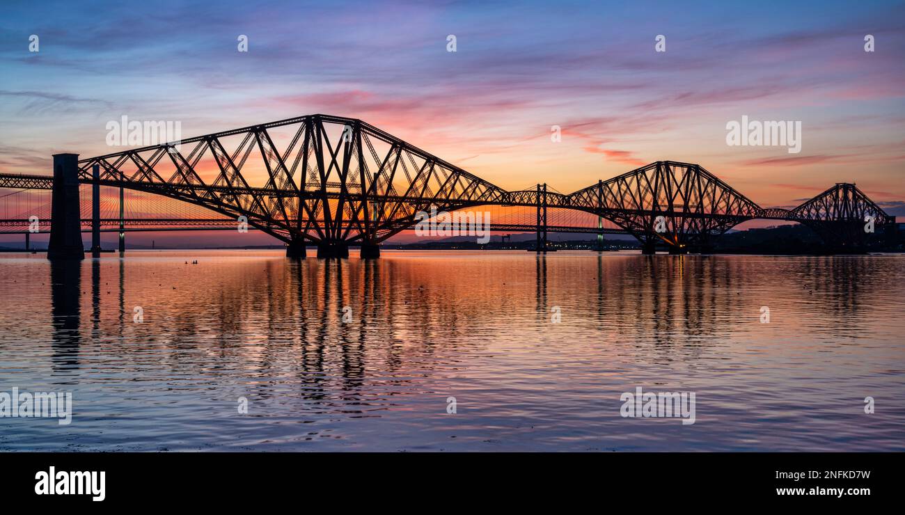 Panoramic view of the Forth Rail Bridge at dusk, with Forth Road Bridge and Queensferry Crossing beyond, from South Queensferry, Scotland, UK Stock Photo