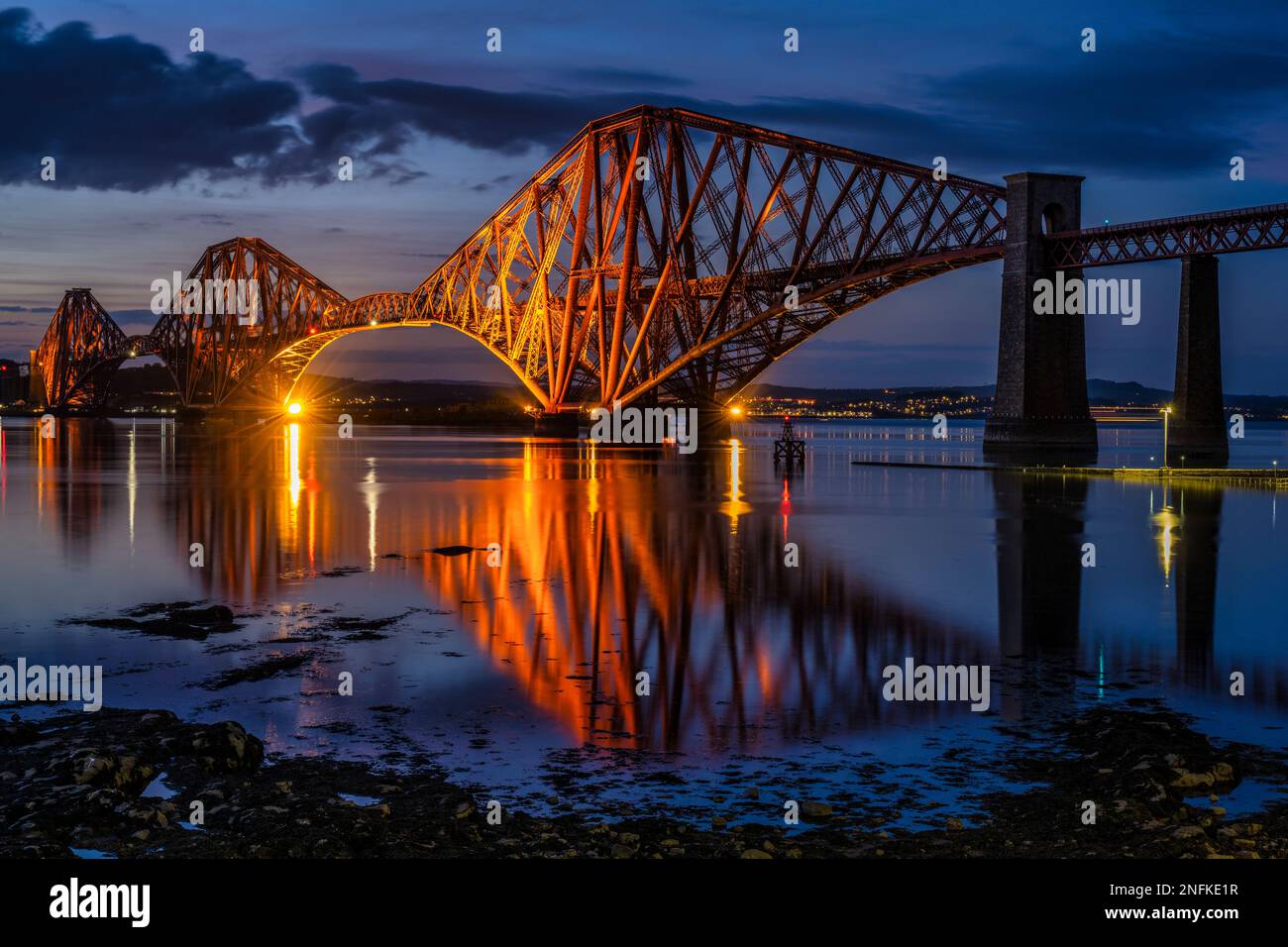 Floodlit Forth Rail Bridge at dusk, with Haws Pier in foreground, from South Queensferry, Scotland, UK Stock Photo