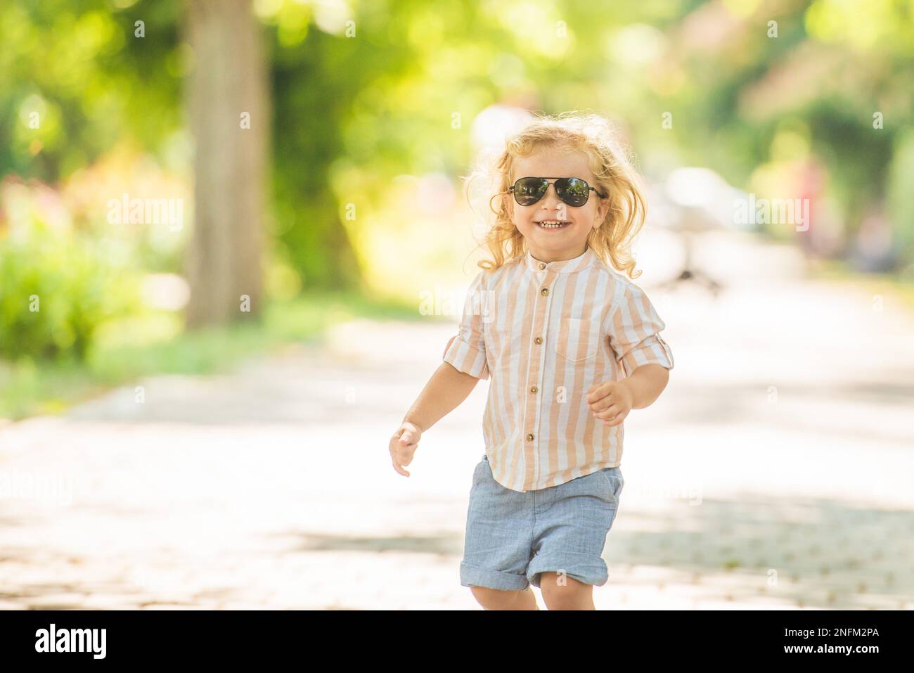 Cute little boy with curly blonde hair playing in park Stock Photo