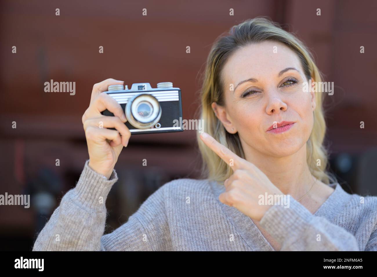 Smiling middle aged woman holding an old camera and pointing a finger at the camera with a twinkling eye Stock Photo