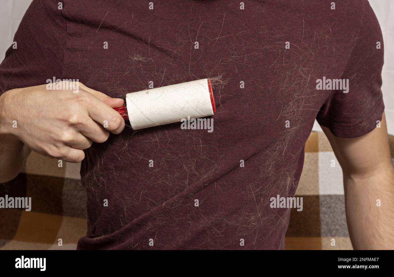 A man with a sticky clothes roller removes animal hair from clothes