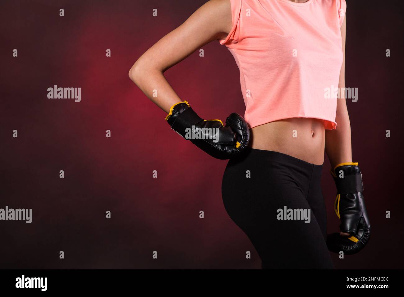 A girl in a pink crop top with boxing gloves on preparing for a training session, isolated on a red background Stock Photo
