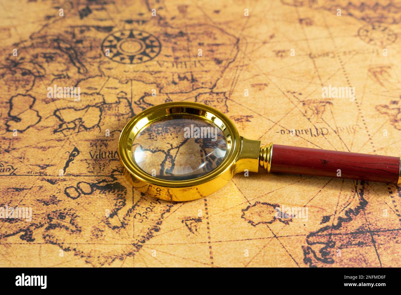 A closeup of a vintage magnifying glass with a gold frame laying on an ...