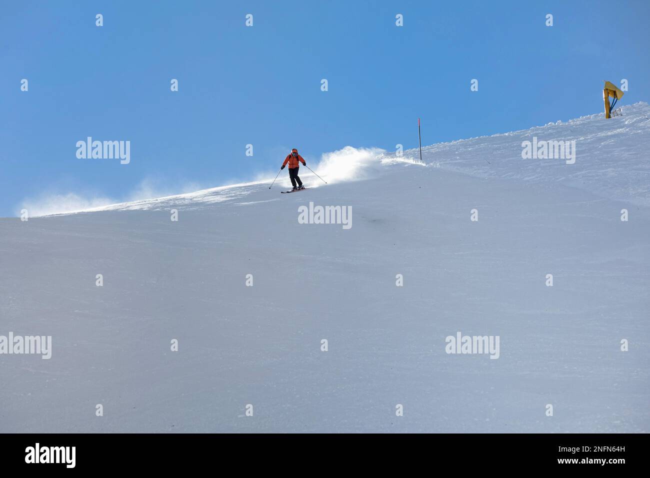 A young female skier in an orange jacket turns carving arches on the slope. A beautiful sunny day in the mountains, on the ski slope, a skier in an or Stock Photo