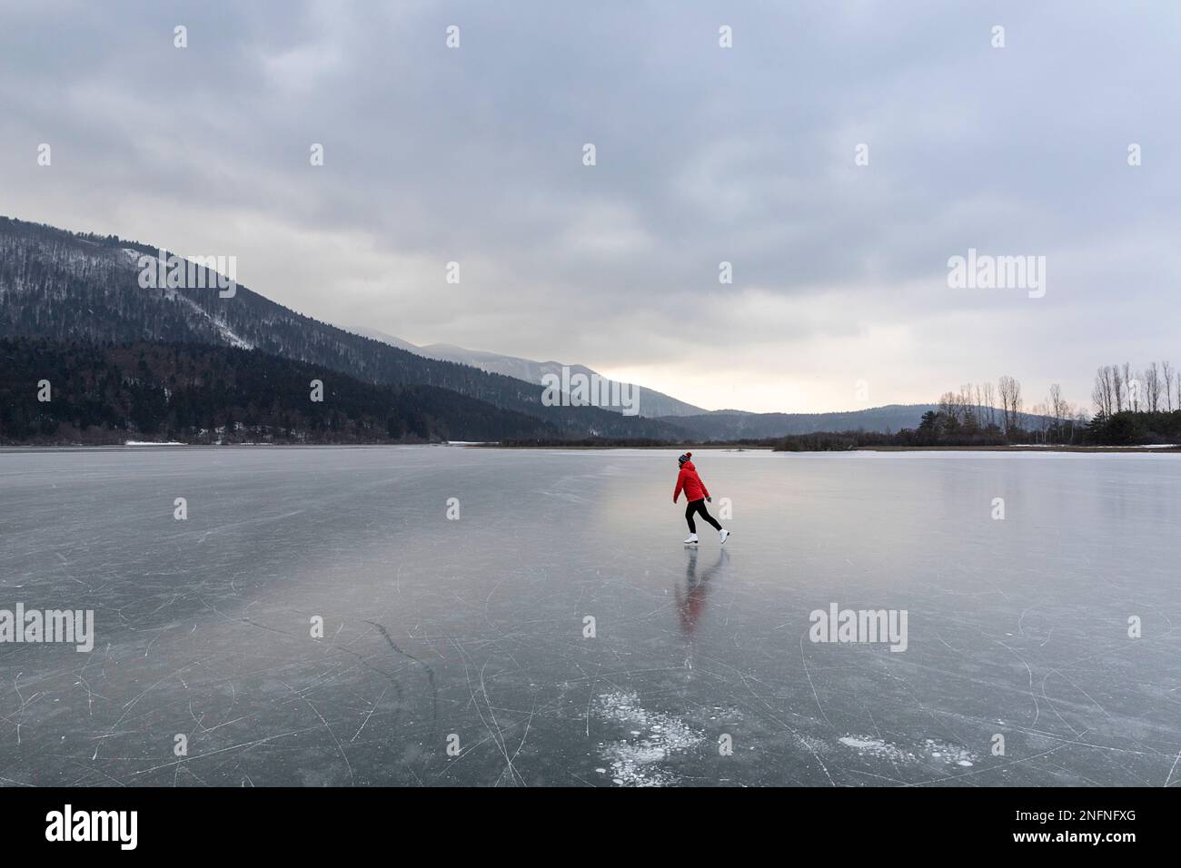 Woman tourist in red jacket ice skating on a spectacular frozen Cerknica lake, biggest intermittent lake in Slovenia, winter recreation in Slovenia Stock Photo