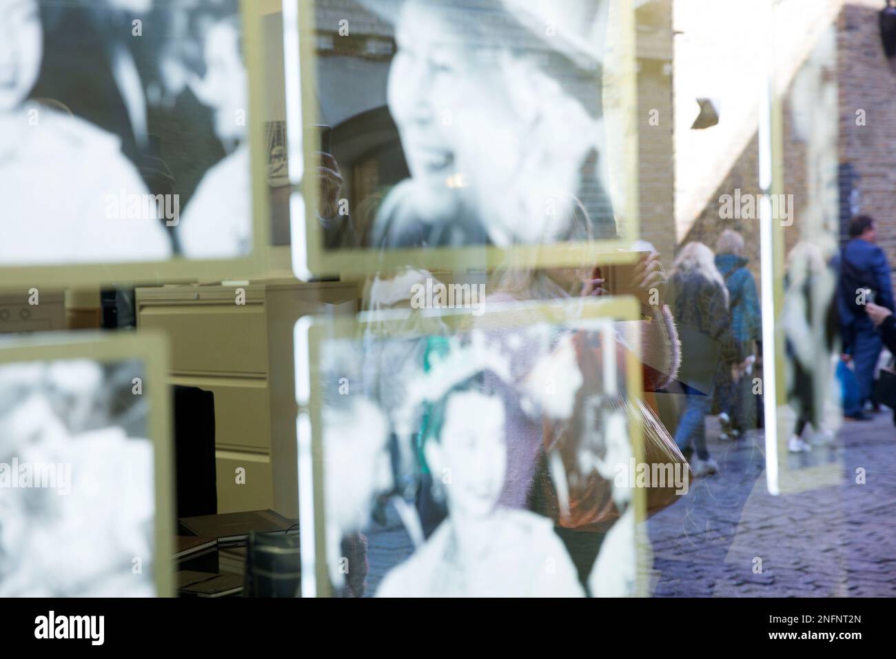 People queuing for the lying-in-state are reflected in a shop window where portraits of the late Queen Elizabeth II are displayed in London. Stock Photo