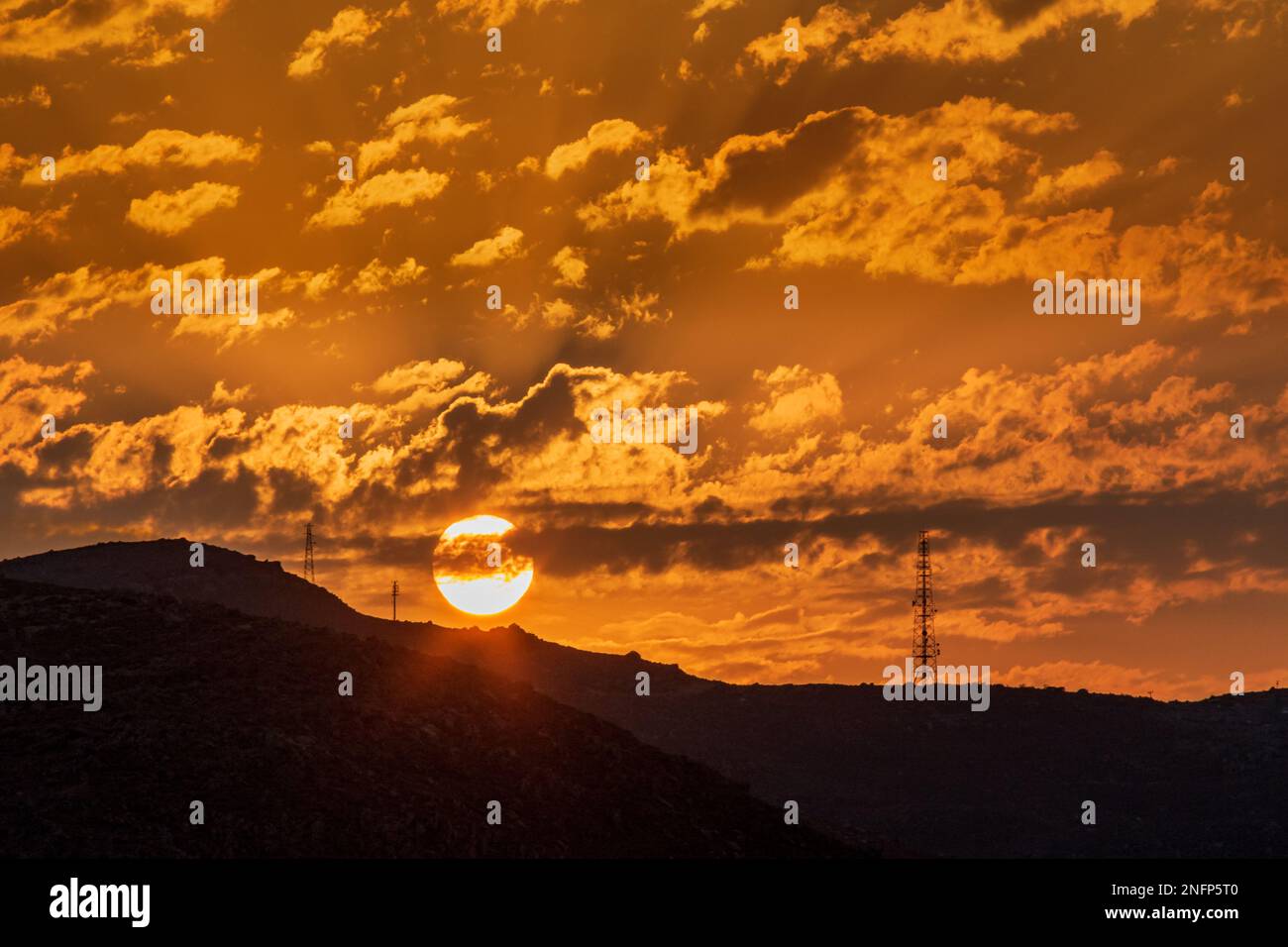 setting sun behind hill with pylons Stock Photo