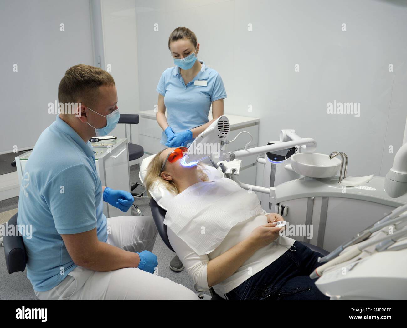 dental clinic teeth whitening woman lying under apparatus doctor and