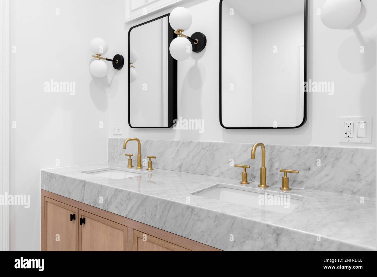A bathroom with a white oak cabinet, marble countertop, gold faucets ...