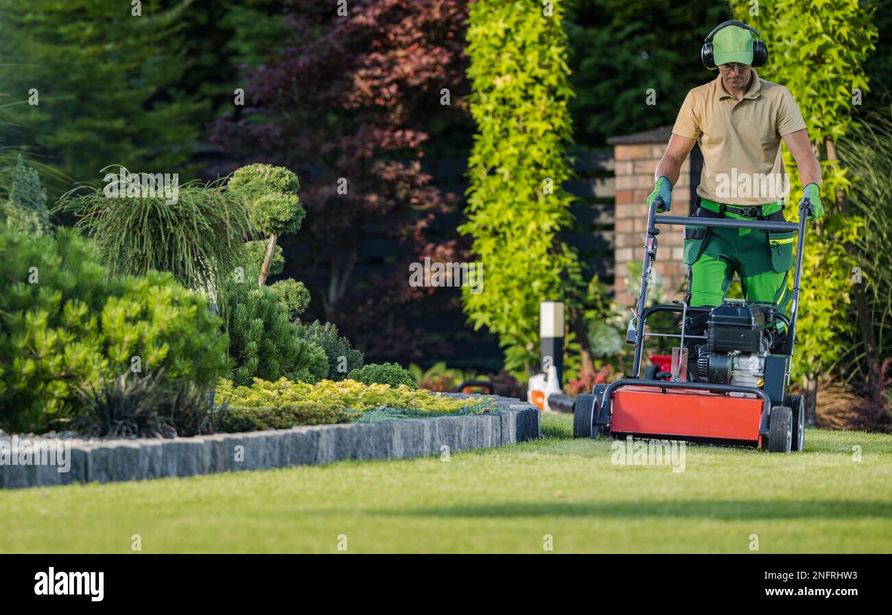 Professional Caucasian Gardener Mowing the Lawn During Backyard Garden Maintenance Work. Gardening Services and Equipment. Stock Photo