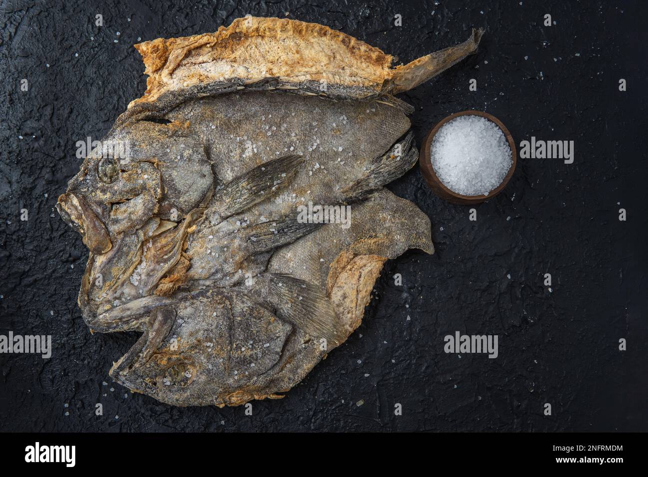 Top view of salted cod on a black stone background with grains of sea salt Stock Photo