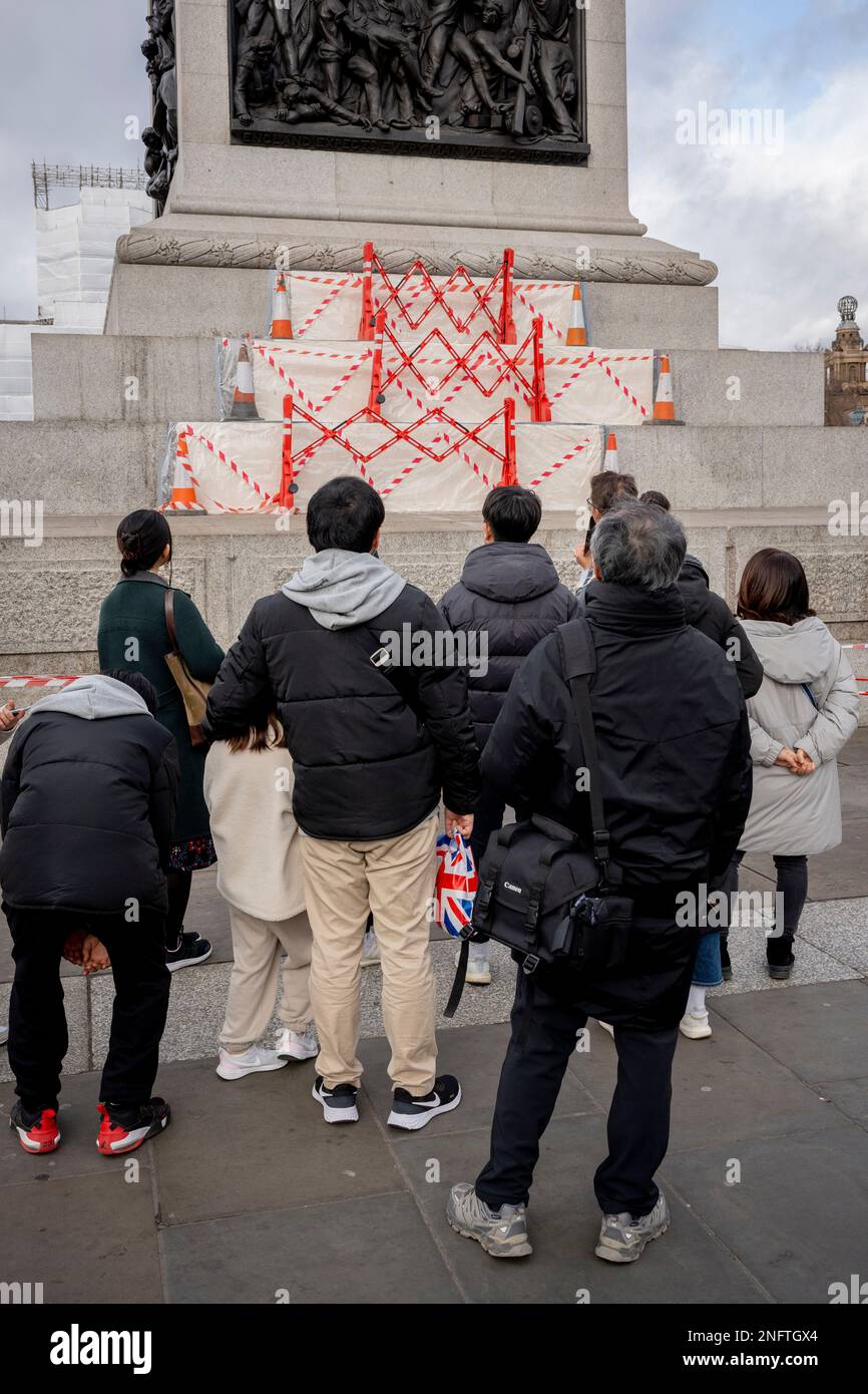 Members of the public listen as part of their tour of the capital, to a guide describing Nelson's Column, beneath hazard tape that covers repairs to granite stonework of the plinth to Nelson's Column in Trafalgar Square, on 17th February 2023, in London, England. Stock Photo