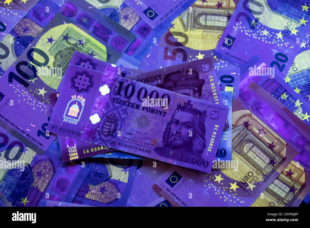 To verify the authenticity of the money. 20,000 HUF banknote in UV light, euro banknotes in the background. The image may contain noise and grain. Stock Photo