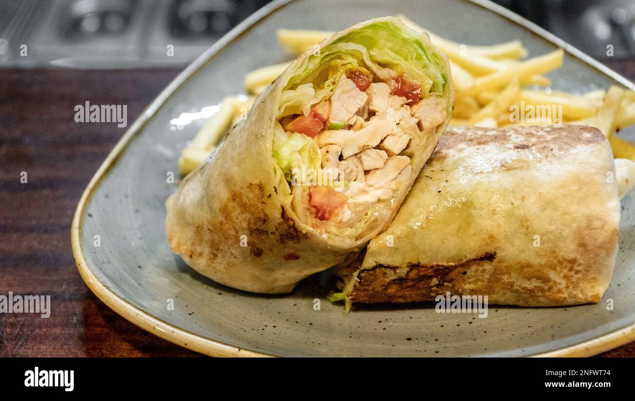 a tasty image of a freshly prepared chicken tortilla wrap filled with salad and served with French fries Stock Photo
