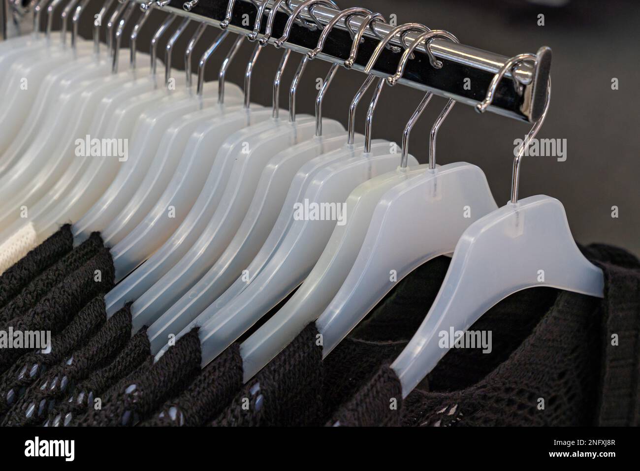 A row of white plastic hangers in a store with a knitted brown jacket hanging on them. Close up. Stock Photo