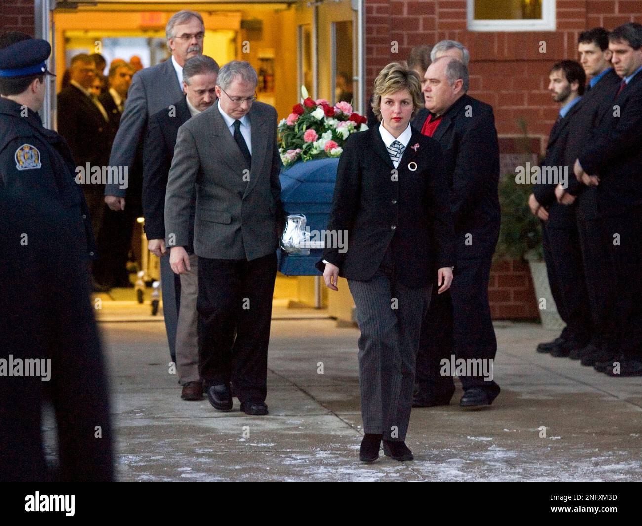 A funeral home worker leads pall bearers as they carry the coffin of