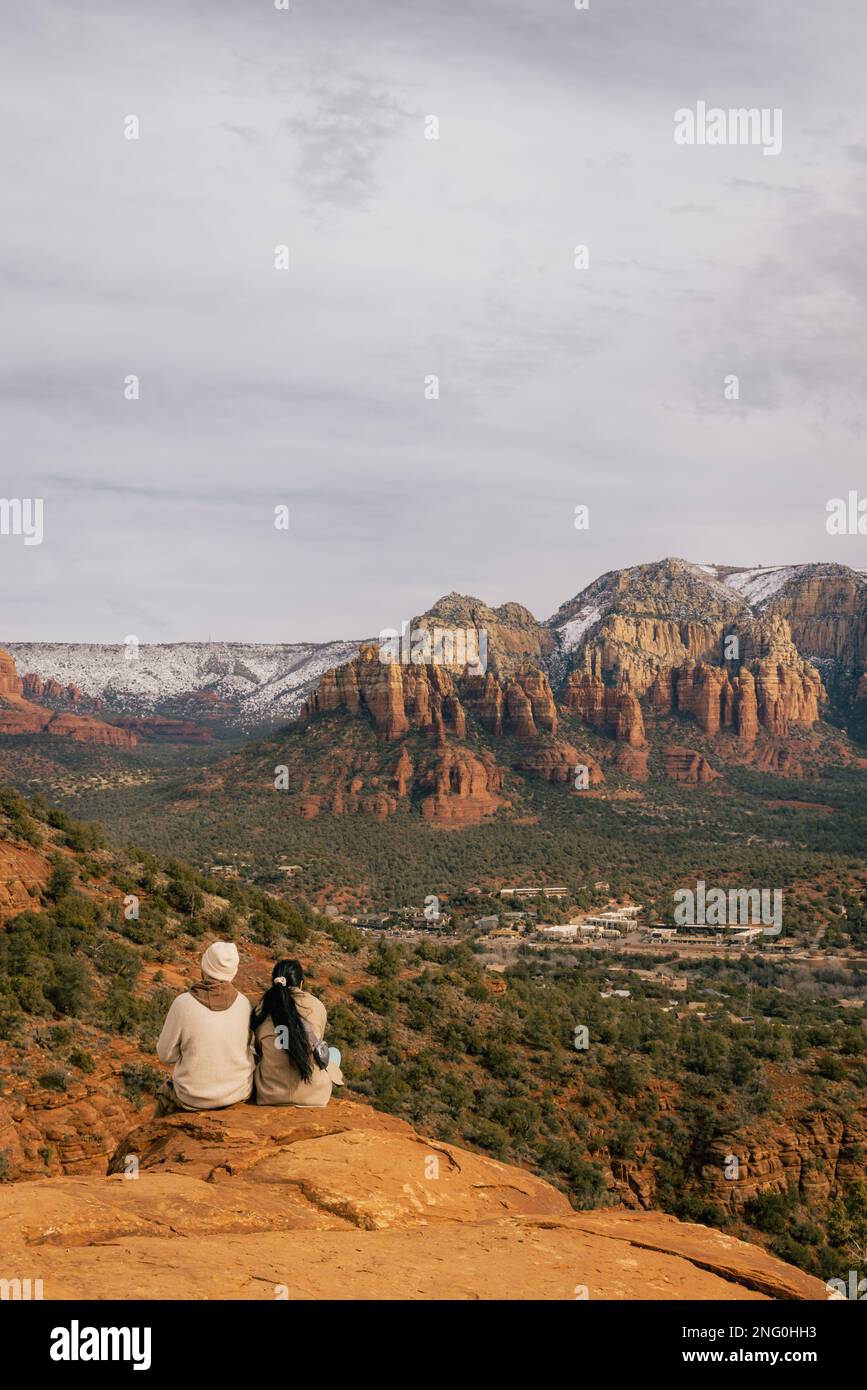 Young heterosexual couple enjoys a sunset viewpoint in Sedona Arizona as seen from Airport Mesa Vortex looking towards red rock mountain cliffs Stock Photo