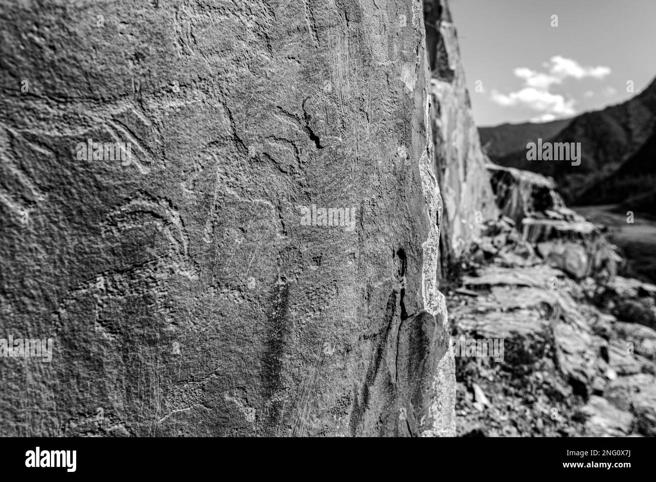 Petroglyphs rock drawing of ancient people animals on stones behind the panorama of the Altai mountains in Siberia. Black and white photo. Stock Photo