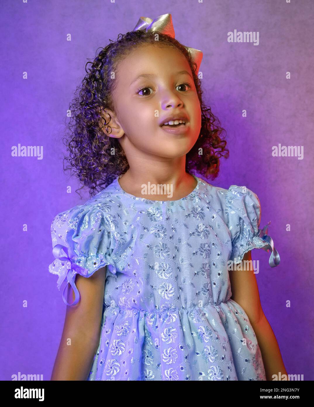 Studio portrait of beautiful little girl in beautiful blue dress singing on purple background Stock Photo