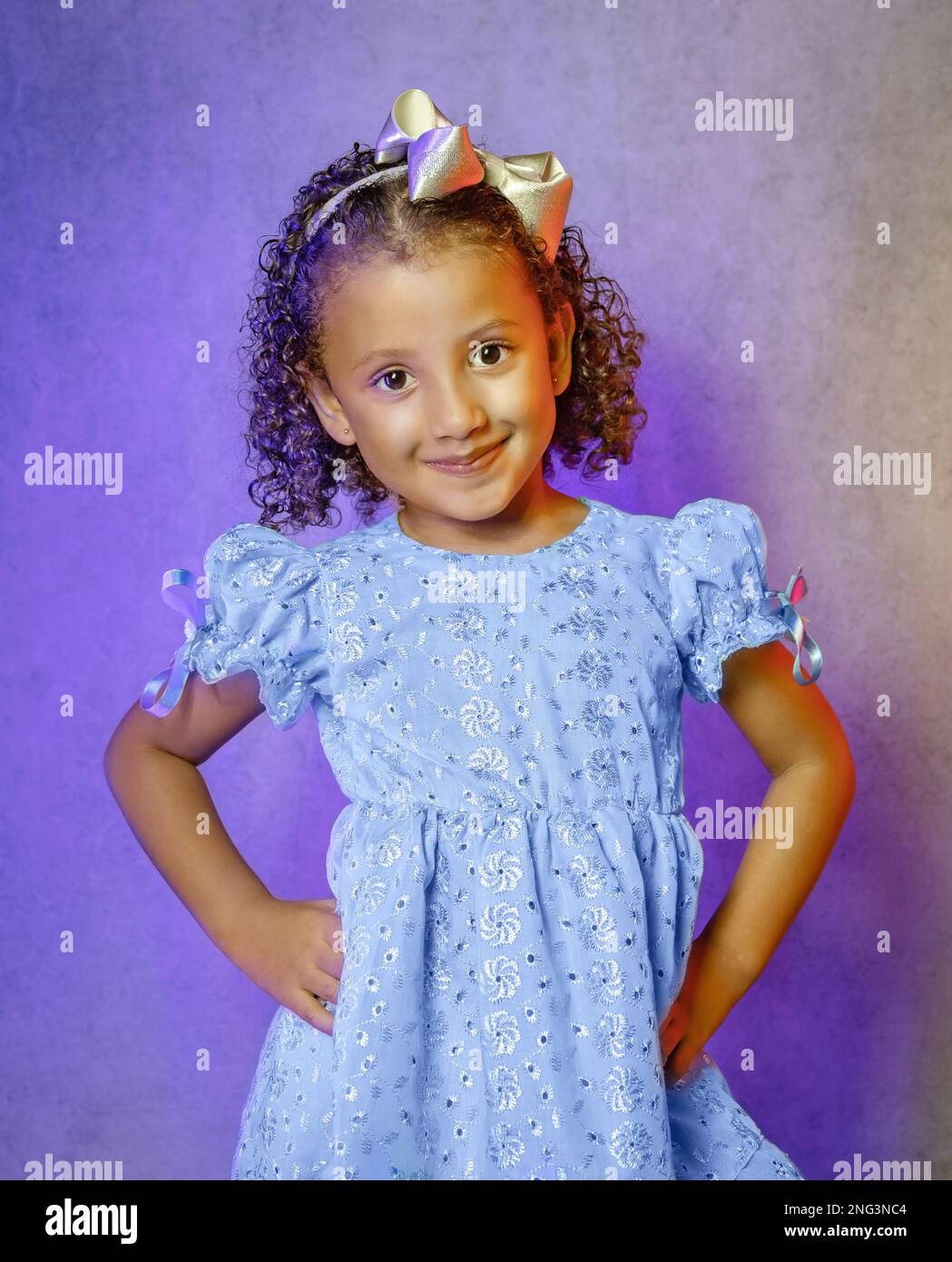 Studio portrait of beautiful little girl in beautiful blue dress on purple background, brazilian girl smiling, giving kisses and making funny faces Stock Photo