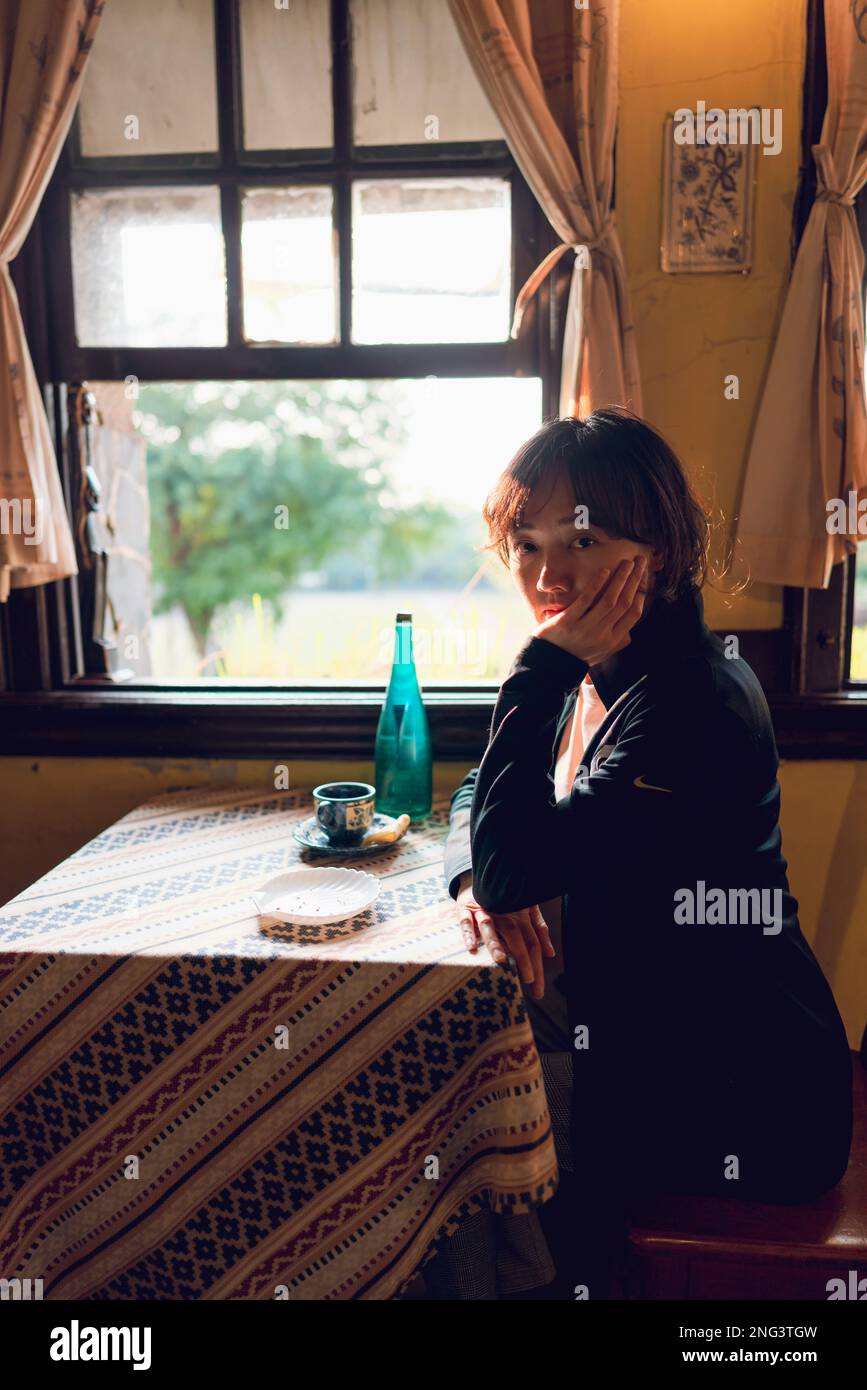 A woman sits by a window. The photo was taken in a cafe that has a retro-style interior. Stock Photo