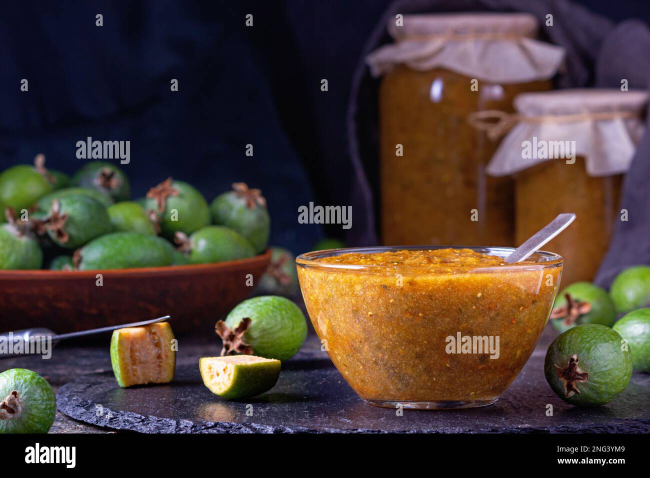 Feijoa jam in a glass bowl with cut green feijoa fruits. Natural homemade dessert. Rural still-life closeup with selective focus Stock Photo