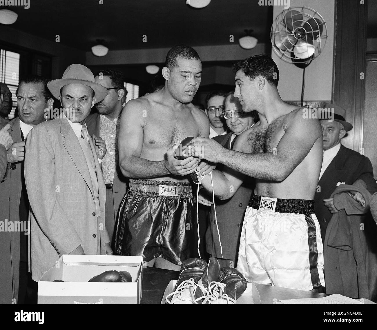 Joe Louis (left) and his opponent, Oct. 26, 1951 in a ten-round heavyweight  bout, Rocky Marciano (right) of Brockton, Mass., check over the gloves they  will wear. Watching (center) is Deputy State