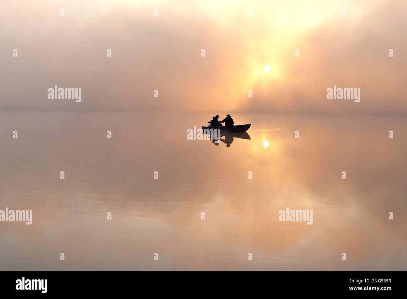 Sunrise in fog Lake Cassidy with fishermen in small fishing boat Stock
