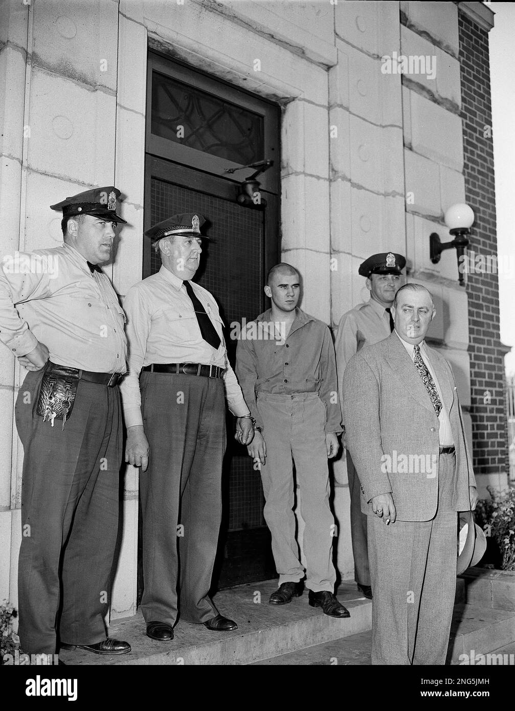 William Heirens, hair shorn, dressed in prison attire and cuffed to prison guards, pauses on the