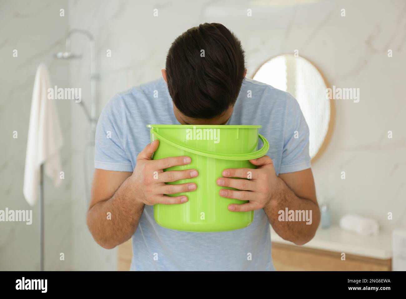 Man with bucket suffering from nausea in bathroom. Food poisoning Stock