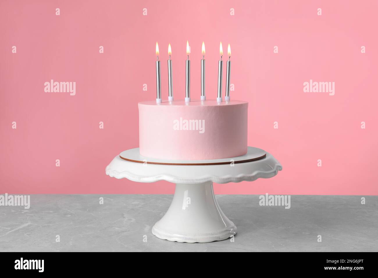 Birthday cake with burning candles on table against pink background ...