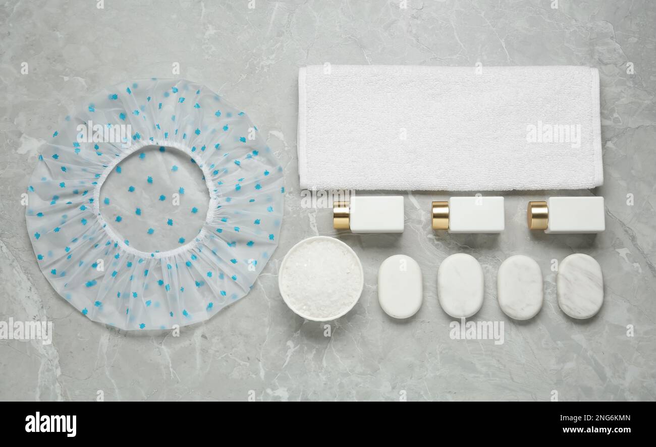 Flat lay composition with shower cap and toiletries on grey marble ...