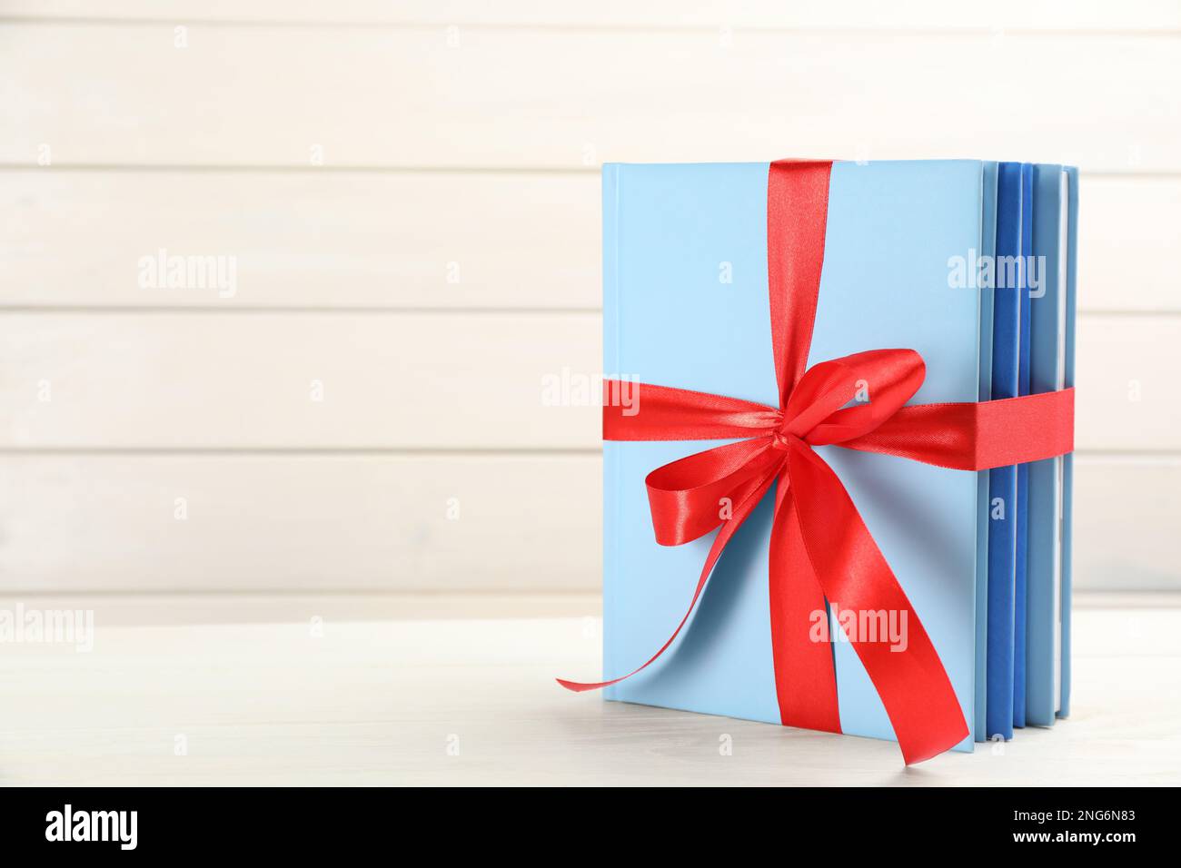 Different books tied with red ribbon on white table, space for text ...