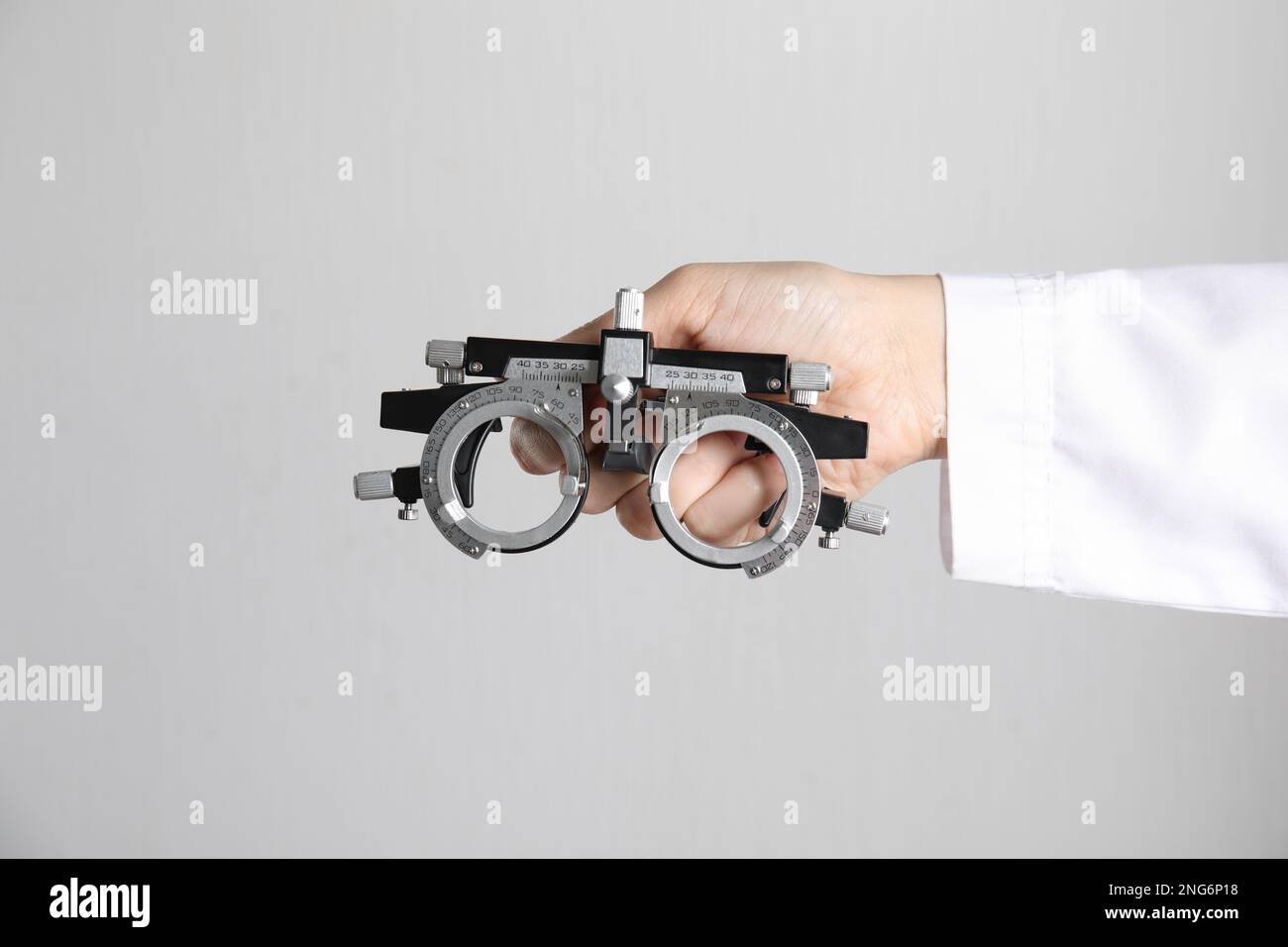 Ophthalmologist holding trial frame on light background, closeup Stock Photo