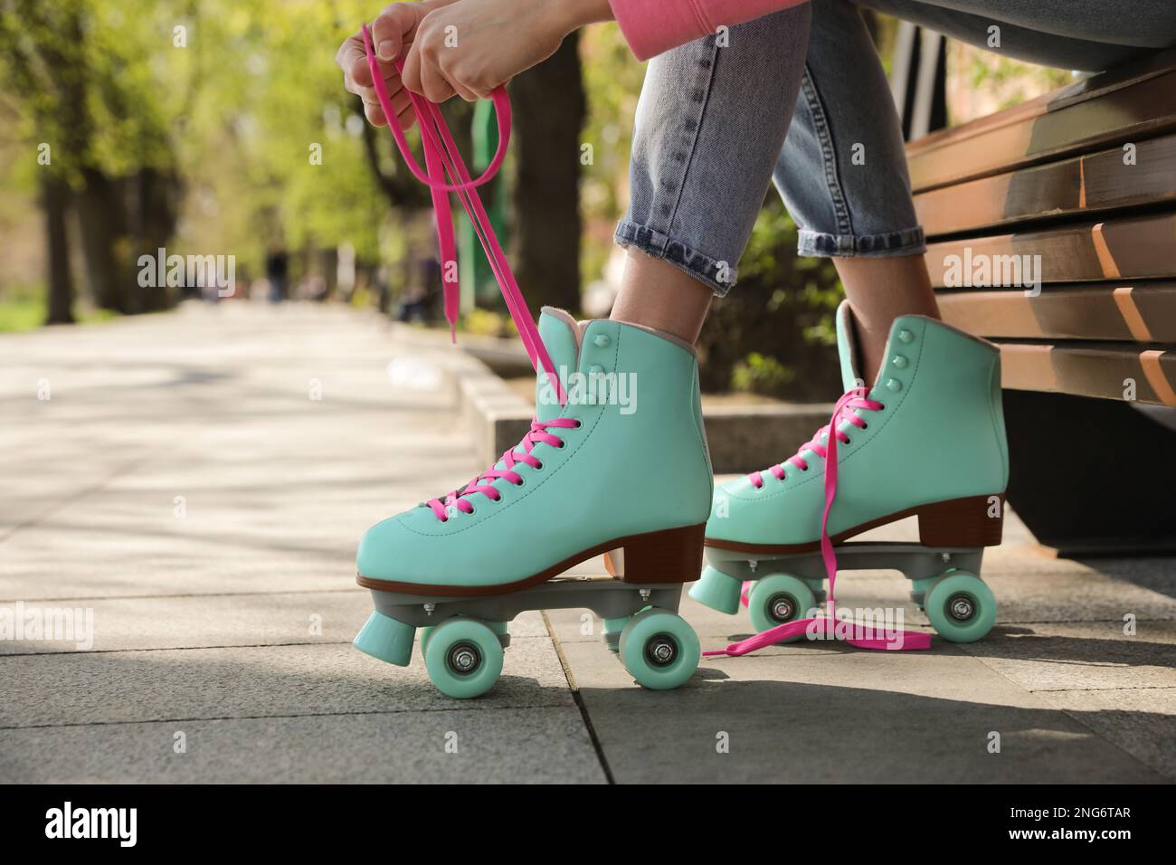 Woman lacing roller skates while sitting on bench outdoors, closeup