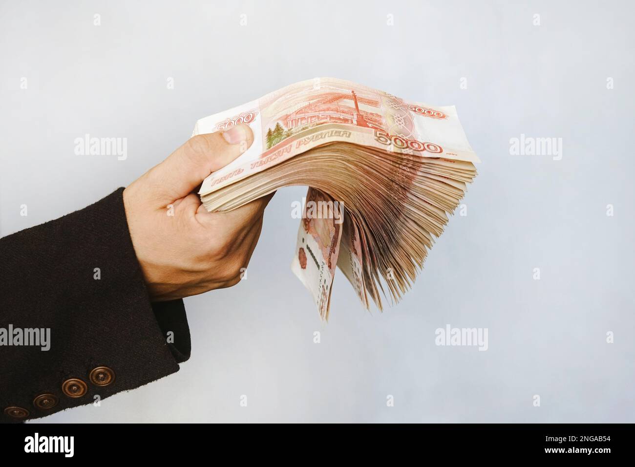 a lot of money in the hand of a young businessman on a blue background. A stack of banknotes of Russian rubles with a face value of 5000 rubles. succe Stock Photo