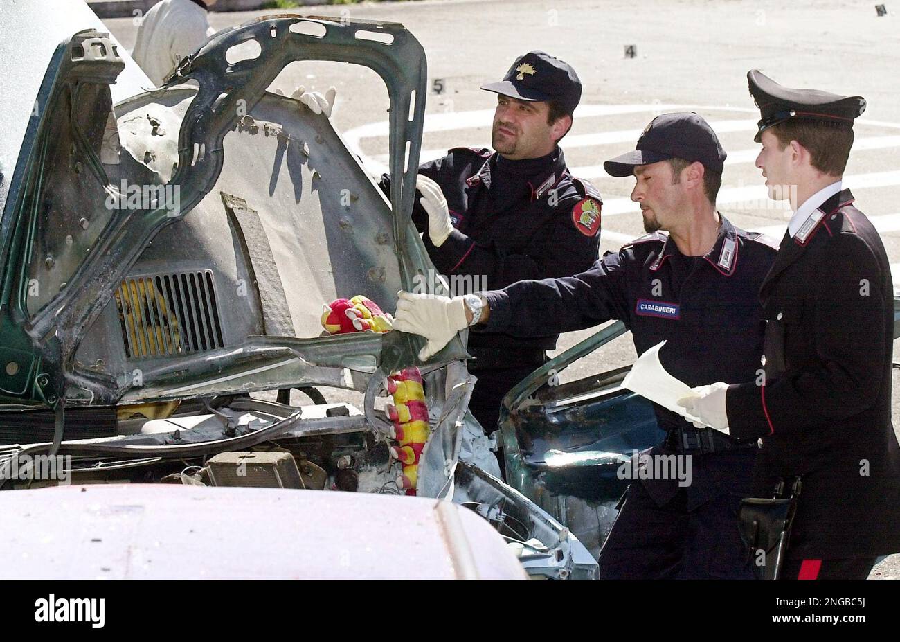 Italian police officers inspect the vehicle destroyed by a remote controlled car bomb placed for