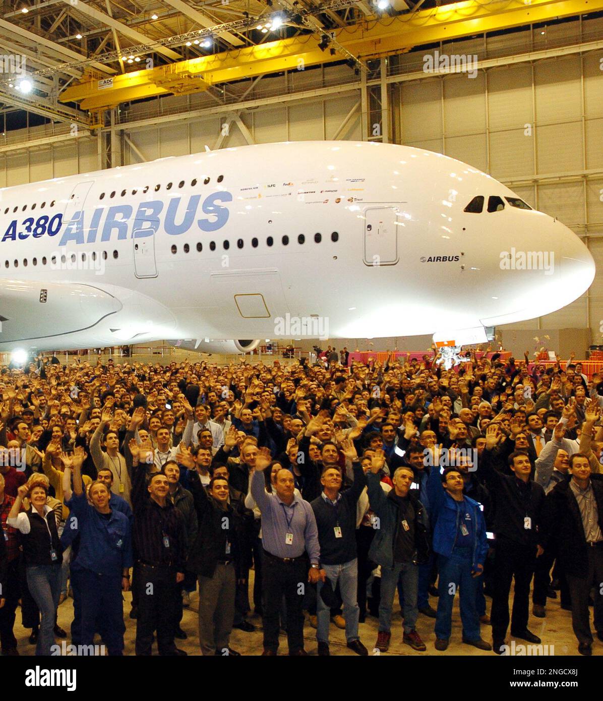 Airbus employees wave next to the new Airbus A380 after its unveiling